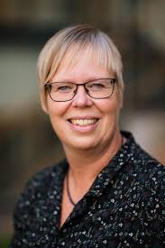 En blond kvinna med svarta glasögon och spräcklig kavaj.