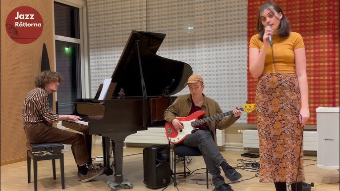 Bandet Jazzråttorna står på en scen. En kvinna sjunger, medan en kille spelar gitarr och en kille spelar piano.