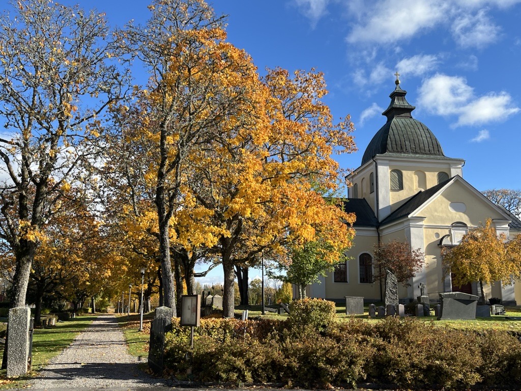 Ervalla gula kyrka med lövträd i höstfärger.