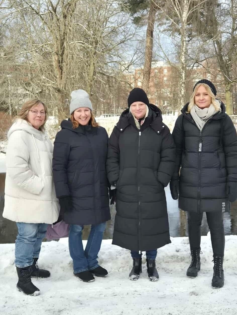Fyra kvinnor står i ett snöigt landskap. I bakgrunden Svartån.