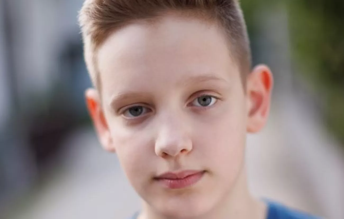 Närbild på en pojke i blå tröja. Det kortklippta håret står rakt upp, sorgsen blick.